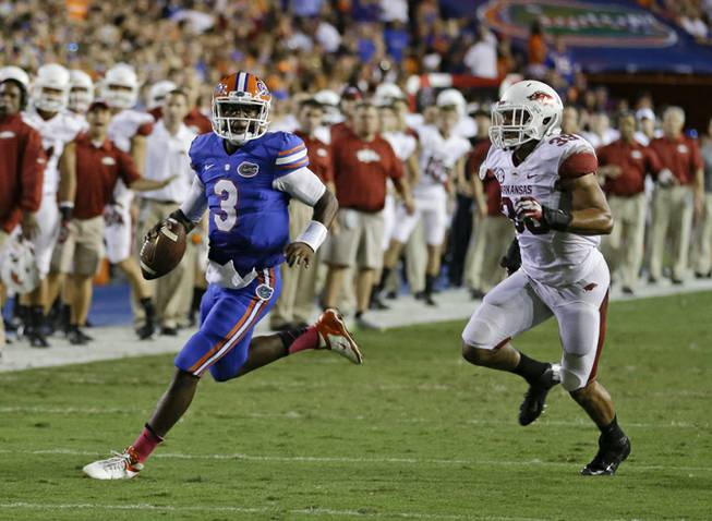 Florida quarterback Tyler Murphy (3) looks for a receiver as he scrambles away from Arkansas linebacker Jarrett Lake, right, during the first half of an NCAA college football game in Gainesville, Fla., Saturday, Oct. 5, 2013.