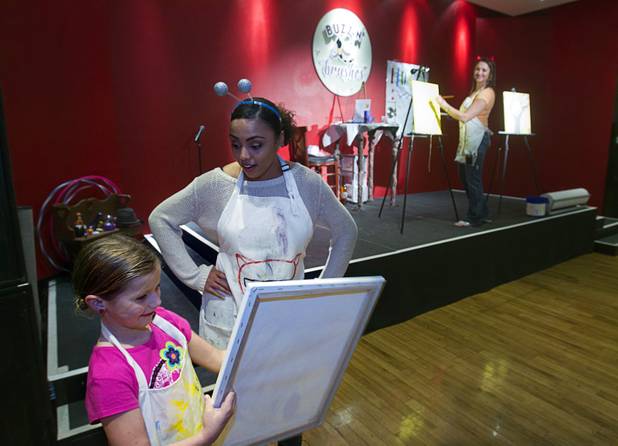 Anna Berry, 9, shows her work to "Beekeeper" Jordan Turner as "BeeExtraordinaire" Caroline App, far right, leads a class at the Buzz'N Brushes art studio in the Orleans Sunday, Oct. 13, 2013.  The studio combines art and entertainment for beginners and shares space with a bar and pizza kitchen.