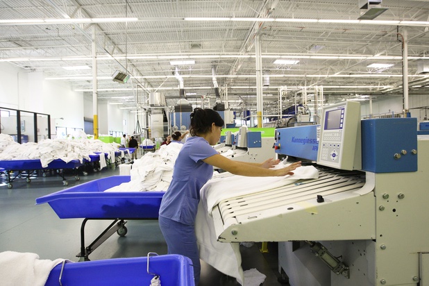 An employee feeds a clean towel into the folding machine during a walk-through of Apex Linen in Las Vegas Tuesday, October 30, 2013.