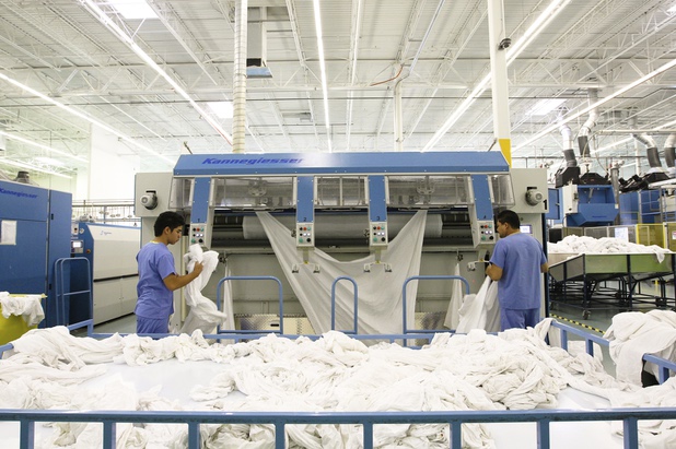Employees clip clean sheets into the ironing machine during a walk-through of Apex Linen in Las Vegas Tuesday, October 30, 2013.