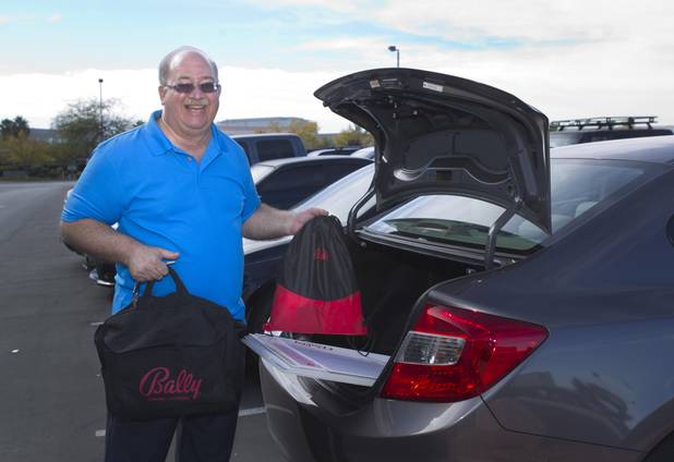 E.J. Coyle, a project manager at Bally Technologies, poses with oversized checks and tools of the trade at the company Thursday, Nov. 14, 2013. One bag holds paperwork and instructions. The other bag is full of Bally Technologies-branded goods. Coyle is a member of the Jackpot Response Team. A member is always on call in the event that a gambler hits a progressive jackpot on a Bally Technologies slot machine.