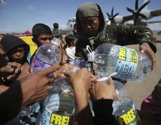 A Filipino trooper distributes water to survivors waiting for a military flight to Manila as they flee typhoon hit Tacloban city, Leyte province, central Philippines on Friday, Nov. 15, 2013. 