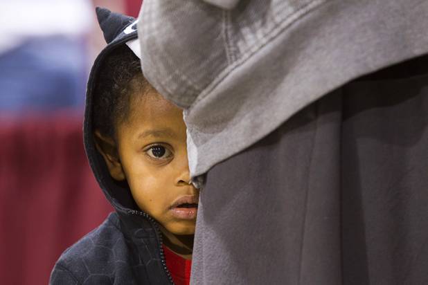 Amir Stewart, 2, hides behind his father's legs as they wait in a line during the Fall 2013 Southern Nevada Project Homeless Connect at Cashman Field Center Tuesday, Nov. 19, 2013. The annual event brings together a variety of social and legal services to help homeless and low-income people.