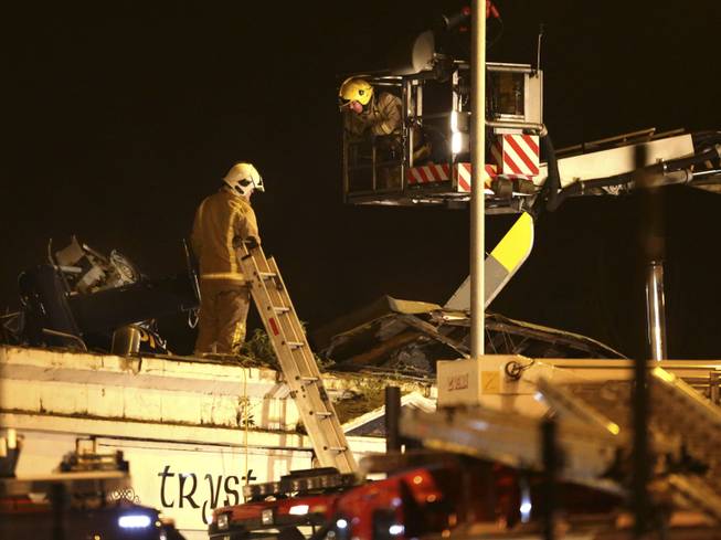 Firefighters inspect the damage at the site of a helicopter crash in Glasgow, Scotland, early Saturday Nov. 30, 2013. The police helicopter crashed late Friday night into the roof of a popular pub, leaving the building littered with debris and emergency crews scrambling to the scene.