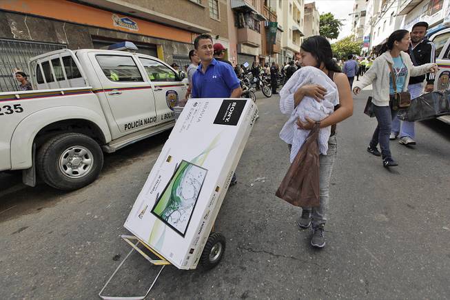 A man carries a newly purchased television on a dolly for a woman outside an appliance store in Caracas, Venezuela, Nov. 13, 2013. President Nicolas Maduro ordered the military to take over appliance stores, slashing prices, leading bargain hunters to form block-long lines across the country. 