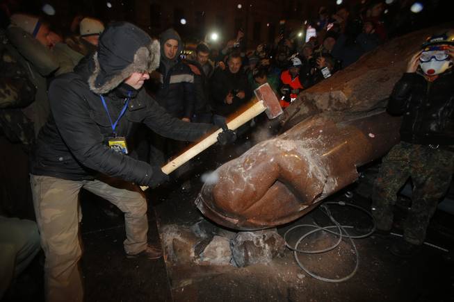 An anti-government protester smashes the statue of Vladimir Lenin with a sledgehammer in Kiev, Ukraine, on Sunday, Dec. 8, 2013. 