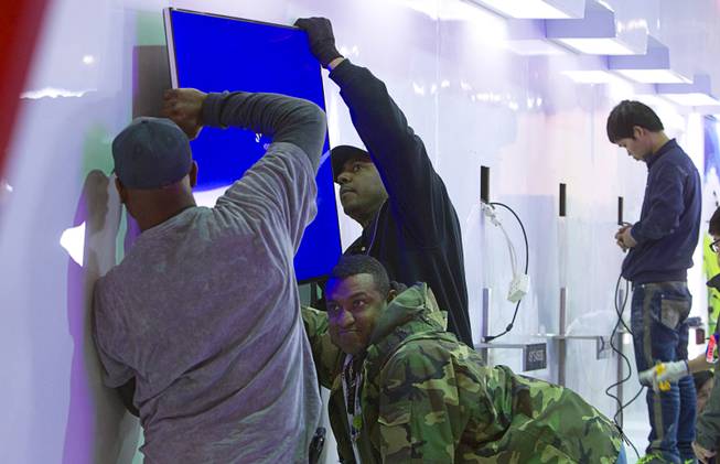 Workers hang a flat screen television as they set up a display in the TCL Communication booth before the 2014 Consumer Electronics Show (CES) at the Las Vegas Convention Center Saturday, Jan. 4, 2014.
