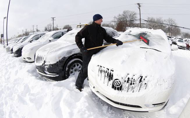 Matt Frame brushes off a Buick at Ray Laethem Buick-GMC in Detroit, Monday, Jan. 6, 2014. Michigan residents are preparing for diving temperatures as they dig out from more than 15 inches of snow in places. 