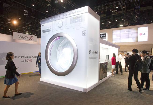 People pass by an oversize mockup of an LG Electronics washer at the LG booth during the 2014 International Consumer Electronics Show (CES) in Las Vegas, Tuesday Jan. 7, 2014.