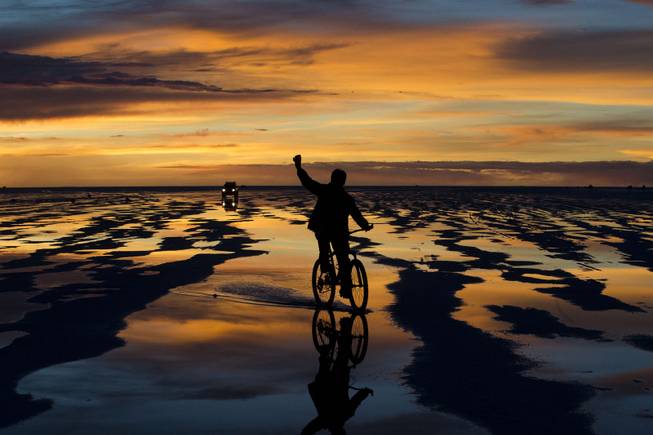 A bicycle rider waves to friends at the Uyuni Salt Flats in Uyuni, Bolivia,  Saturday, Jan. 11, 2014. The motorcycles and quads of the Dakar Rally will race through parts of the Uyuni Salt Flats on Jan. 13, 2014. 