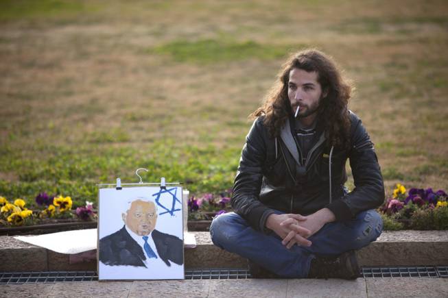 An Israeli man sits next to a painting of former Israeli Prime Minister Ariel Sharon near his coffin at the Knesset plaza, in Jerusalem on Sunday, Jan. 12, 2014. Sharon, the hard-charging Israeli general and prime minister who was admired and hated for his battlefield exploits and ambitions to reshape the Middle East, died Saturday, eight years after a stroke left him in a coma from which he never awoke. He was 85.