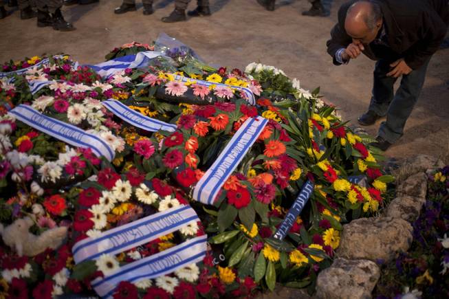 An man mourns next to the flower-covered fresh grave of late Israeli Prime Minister Ariel Sharon in Havat Shikmim near Sderot, southern Israel, Monday, Jan. 13, 2014. 