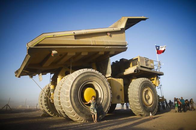 A woman poses next to a giant mining truck at the entrance of the Dakar Rally camp in Calama, Chile, Monday, Jan. 13, 2014. The truck operates in copper mines near the city. 
