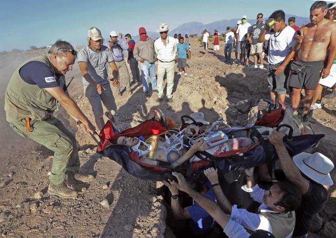 Dakar Rally Director Etienne Lavigne, left, helps carry Suzuki rider Gilbert  Escale of Spain after suffering an accident during the fifth stage of the Dakar Rally between the cities of Chilecito and San MIguel de Tucuman, Argentina, Thursday, Jan. 9, 2014.