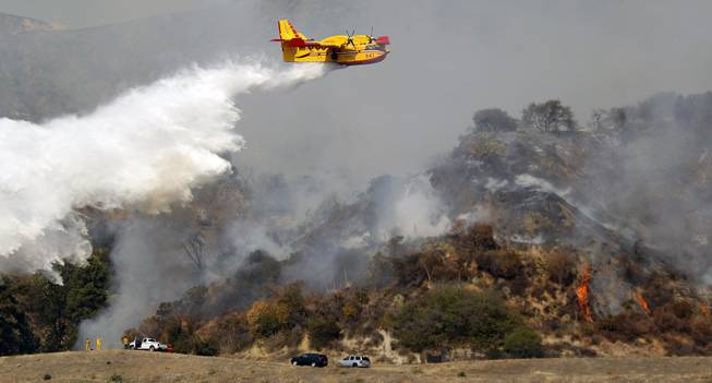 A firefighting plane makes a water drop on a wildfire that's burning in the hills just north of the San Gabriel Valley community of Glendora, Calif., on Thursday, Jan 16, 2014. Southern California authorities have ordered the evacuation of homes at the edge of a fast-moving wildfire burning in the dangerously dry foothills of the San Gabriel Mountains. 