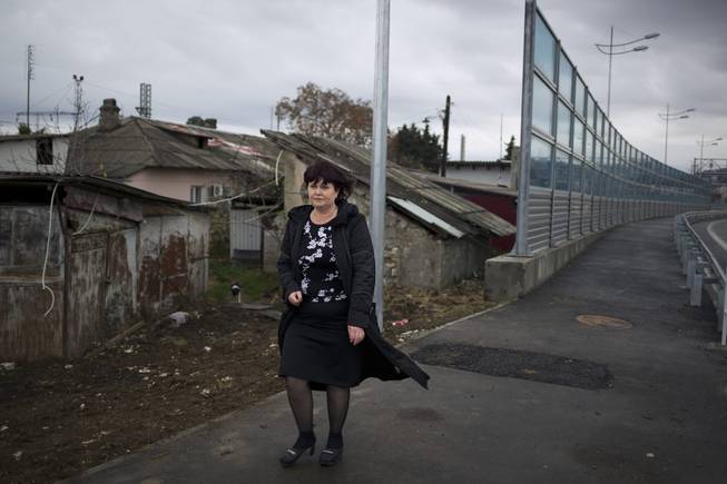 In this photo taken Wednesday, Nov. 27, 2013, Irina Kharchenko walks away from a screen separating the yard of her house and a federal highway in the village of Vesyoloye outside Sochi, Russia.