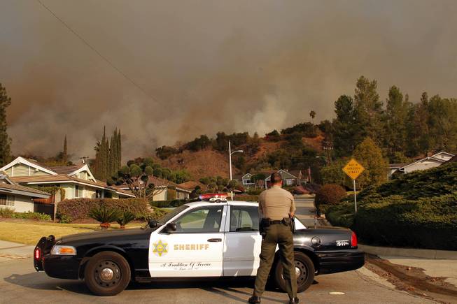 An Los Angeles County Sheriff blocks a road in a neighborhood while a wildfire burns in the hills just north of the San Gabriel Valley community of Glendora, Calif., on Thursday, Jan 16, 2014. 