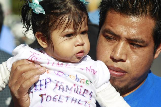 Alejandro Estrada holds his daughter Ruby Estrada as they protest U.S. House Speaker John Boehner as he makes a fundraising appearance for Nevada Rep. Joe Heck at the Las Vegas Country Club Friday, Jan. 17, 2014.