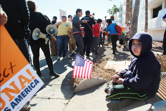 A boy who would only give his name as Jose sits with a flag while his caretaker protests U.S. House Speaker John Boehner as he makes a fundraising appearance for Nevada Rep. Joe Heck at the Las Vegas Country Club Friday, Jan. 17, 2014.