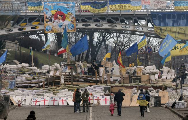 People walk past a barricade in Independence Square in Kiev, Ukraine, Monday, Dec. 23, 2013. Ukraine has been stricken with mass protests for over a month.  Protesters are demanding President Viktor Yanukovych's resignation over his decision to ditch a pact with the European Union in favor of closer ties with Russia.