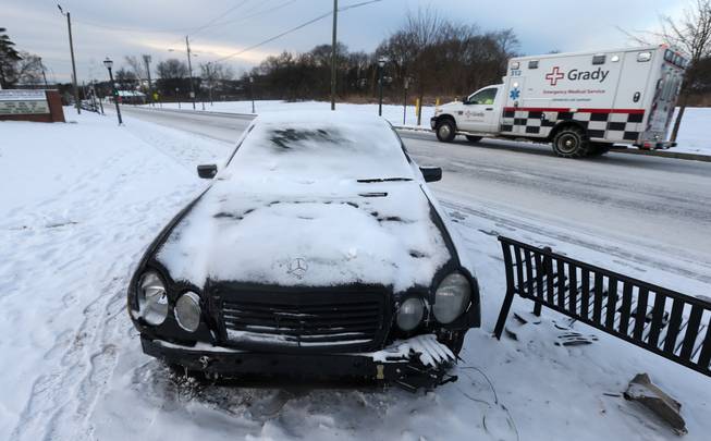 A damaged car is left on the side of the road, stuck in snow off Pryor Road, Wednesday, Jan. 29, 2014, in Atlanta.
