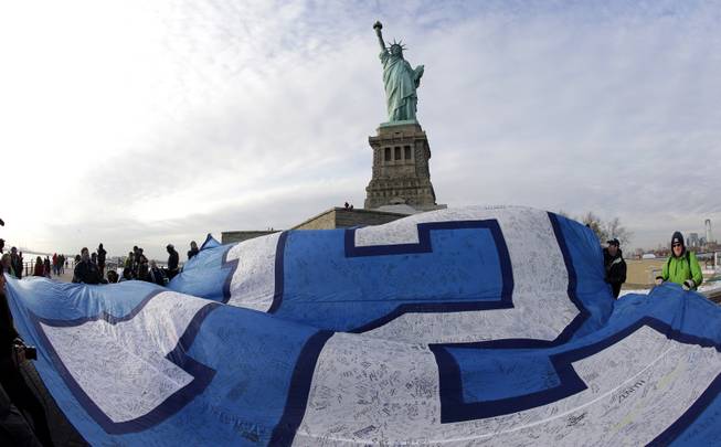 A giant Seattle Seahawks "12th Man" flag that flew on the Space Needle before being signed by fans and brought to New York, is displayed at the Statue of Liberty, Friday, Jan. 31, 2014 in New York. The flag will be given to the Seahawks team as a gift from their fans before they play the Denver Broncos Sunday in the NFL Super Bowl XLVIII football game in East Rutherford, N.J. 