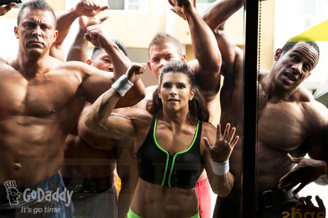 In this image released by GoDaddy.com on Wednesday, Jan. 22, 2014, NASCAR driver Danica Patrick, in a muscle suit, appears with bodybuilders in a Super Bowl XLVIII ad shot in Long Beach, Calif. The ad is expected to air after halftime.
