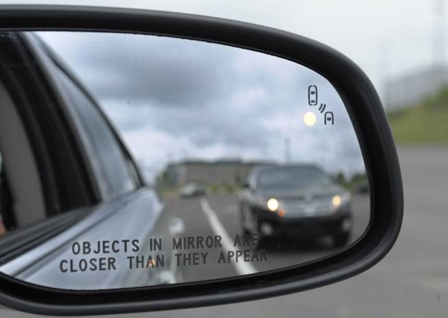 This May 22, 2012, file photo shows a side mirror warning signal in a Ford Taurus at an automobile testing area in Oxon Hill, Md. Federal officials want automakers to equip new cars and light trucks with technology that enables vehicles to communicate with each other to prevent collisions.