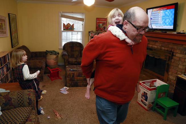 Mike Beck carries his daughter Veronica on his back through the family's living room as his daughter Maria, left, plays a video while trying to combat cabin fever, Monday, Feb. 3, 2014, in Indianapolis. 