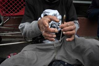 A drug addict prepares a needle to inject himself with heroin in front of a church in the Skid Row area of Los Angeles, Monday, May 6, 2013. It's not a rare scene on Skid Row to spot addicts using drugs in the open, even when police patrol the area. 