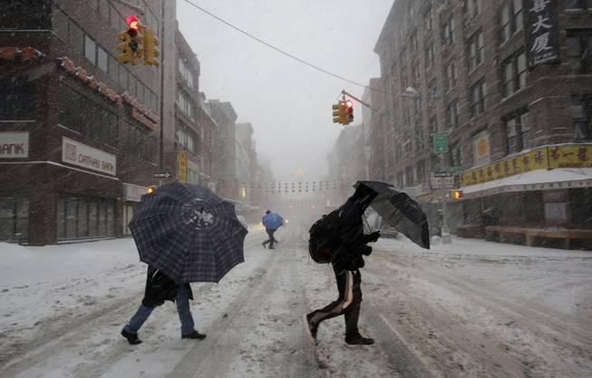 Pedestrians use umbrellas as they walk through falling snow in the Chinatown neighborhood of New York, Thursday, Feb. 13, 2014. Snow and sleet are falling on the East Coast from North Carolina to New England a day after sleet, snow and ice bombarded the Southeast.