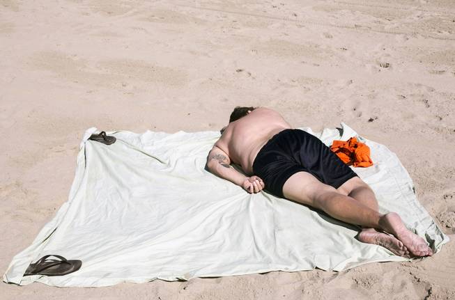 A man rests on the Venice Beach area of Los Angeles, Friday, Feb. 14, 2014. With much of the Northeast gripped by snow and ice storms, the Southwest is riding a heat wave that is setting record high temperatures and sent people to beaches and golf courses in droves Friday. (AP Photo/Damian Dovarganes)