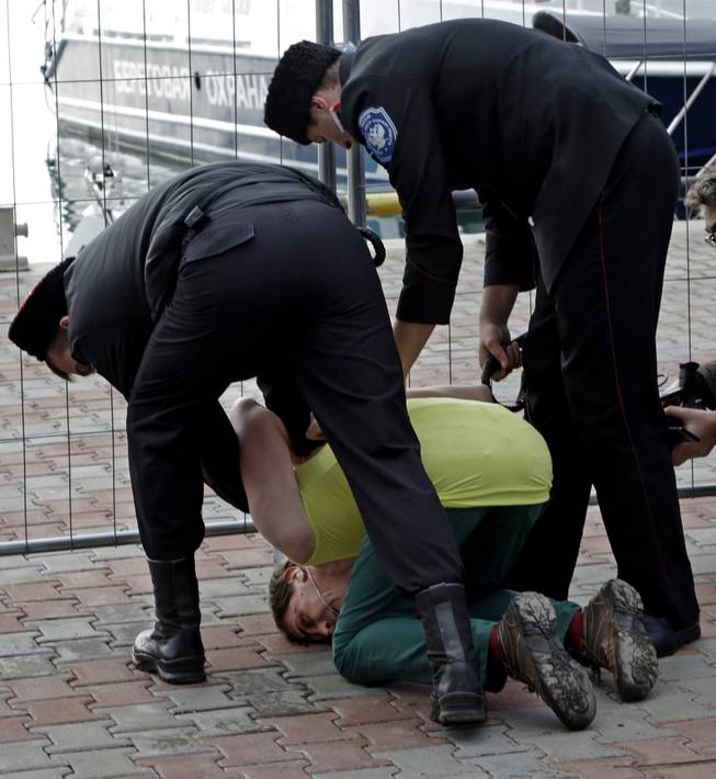 A member of the punk group Pussy Riot is restrained by Cossack militia after the group tried to perform in Sochi, Russia, on Wednesday, Feb. 19, 2014. 