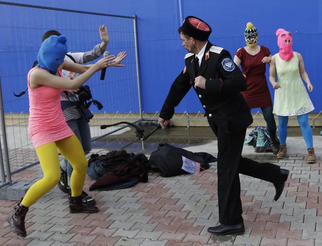 A Cossack militiaman attacks Nadezhda Tolokonnikova and a photographer as she and fellow members of the punk group Pussy Riot, including Maria Alekhina, right, in the pink balaclava, stage a protest performance in Sochi, Russia, on Wednesday, Feb. 19, 2014.