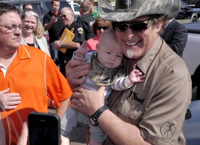 Three-month-old James Bodiford of Lavon, Texas, is photographed with rocker Ted Nugent, right, as Nugent visits with fans during a stop at a local restaurant, Tuesday, Feb. 18, 2014, in Denton, Texas. Nugent and Texas gubernatorial candidate Greg Abbott stopped to promote early voting.