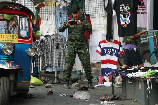 A soldier photographs the scene of an explosion littered with blood and small pairs of shoes at a main protest site in Bangkok, Thailand, Sunday, Feb. 23, 2014. More than a dozen people were hurt Sunday by a small explosion at an anti-government protest in Bangkok, less than a day after a bloodier attack in an eastern province killed one child and left about three dozen people wounded.