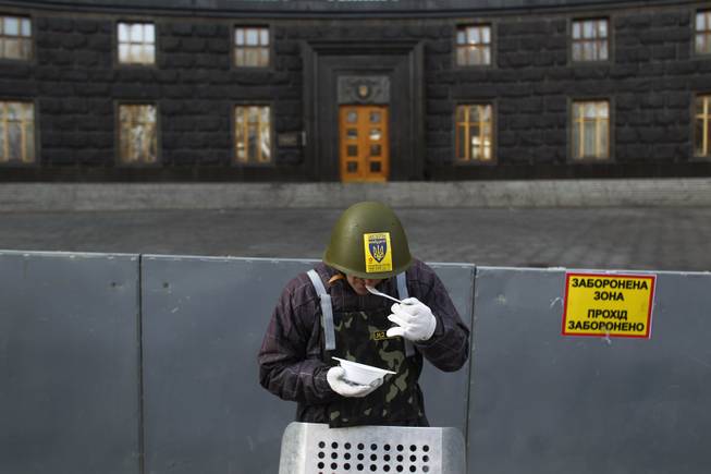 A protester eats as he stands guard in front of the Ukrainian government building in Kiev, Ukraine, Monday, Feb. 24, 2014. 
