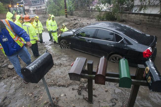 Workers try to help a woman to get her car unstuck from the mud brought by the rain along a hillside in Glendora, Calif., on Friday, Feb. 28, 2014.