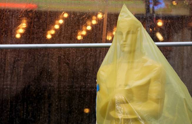 An Oscar statue covered in plastic stands on the red carpet as preparations are made during rainy weather for the 86th Academy Awards in Los Angeles, Friday, Feb. 28, 2014. The Academy Awards will be held at the Dolby Theatre on Sunday, March 2.