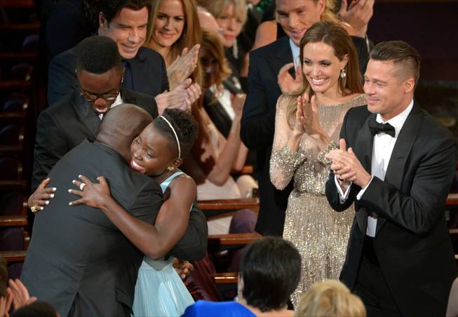 Director Steve McQueen, left, congratulates Lupita Nyong'o on her win for best actress in a supporting role for "12 Years a Slave" as her brother Peter, background from left, and actors John Travolta, Kelly Preston, Benedict Cumberbatch, Angelina Jolie and Brad Pitt, look on, during the Oscars at the Dolby Theatre on Sunday, March 2, 2014, in Los Angeles.  (Photo by John Shearer/Invision/AP)