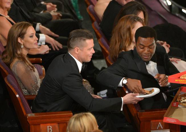 Angelina Jolie, left, looks on as Brad Pitt shares a slice of pizza with Chiwetel Ejiofor in the audience during the Oscars at the Dolby Theatre on Sunday, March 2, 2014, in Los Angeles.  (Photo by John Shearer/Invision/AP)