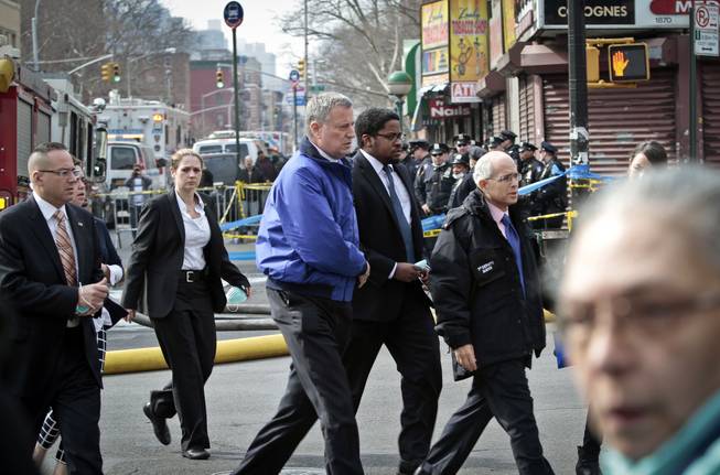Mayor Bill de Blasio, center, arrives to visit the site of an explosion that leveled two apartment buildings in the East Harlem neighborhood of New York, Wednesday, March 12, 2014. Con Edison spokesman Bob McGee says a resident from a building adjacent to the two that collapsed reported that he smelled gas inside his apartment, but thought the odor could be coming from outside.