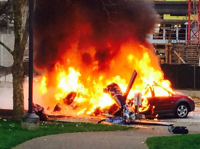 In this photo provided by KOMO-TV, a car burns at the scene of a helicopter crash outside the KOMO-TV studios near the space needle in Seattle on Tuesday, March 18, 2014.