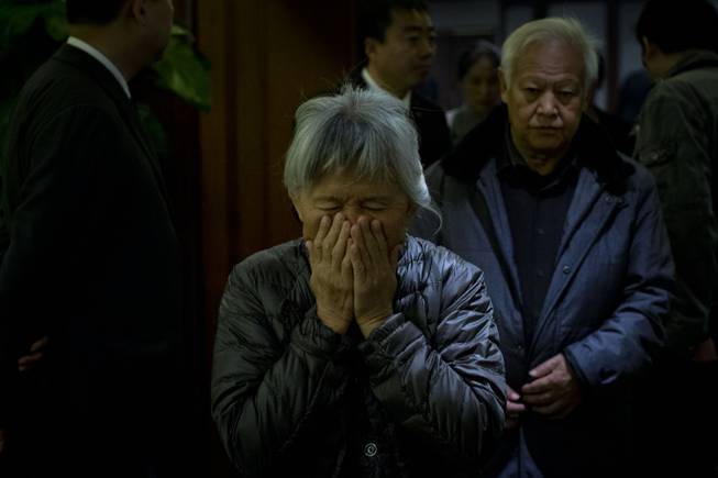 An elderly woman, one of the relatives of Chinese passengers aboard missing Malaysia Airlines Flight MH370, covers her face out of frustration as she leaves a hotel ballroom after a daily briefing meeting with managers of Malaysia Airlines in Beijing, China, Wednesday, March 19, 2014. 