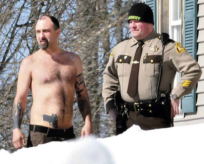 In this Tuesday, March 18, 2014, photo, Michael Smith, left, stands beside a Somerset County Sheriff deputy outside his home in Norridgewock, Maine.