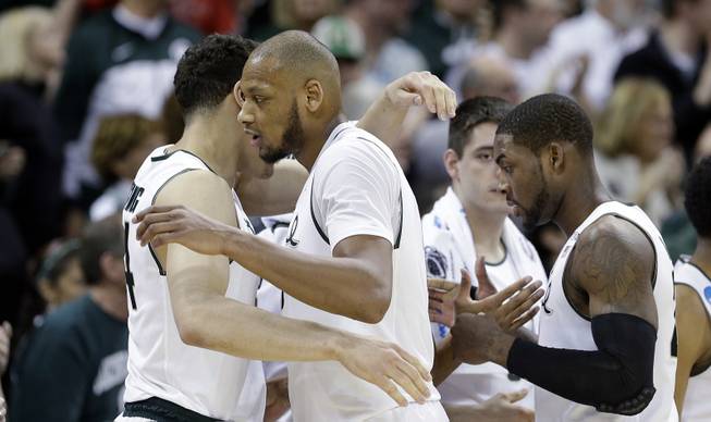 Michigan State's Adreian Payne, center, and Branden Dawson, right, are greeted with hugs as they head to the bench in the final moments of the second half during the second round of the NCAA men's college basketball tournament against Delaware in Spokane, Wash., Thursday, March 20, 2014. Michigan State won 93-78. 