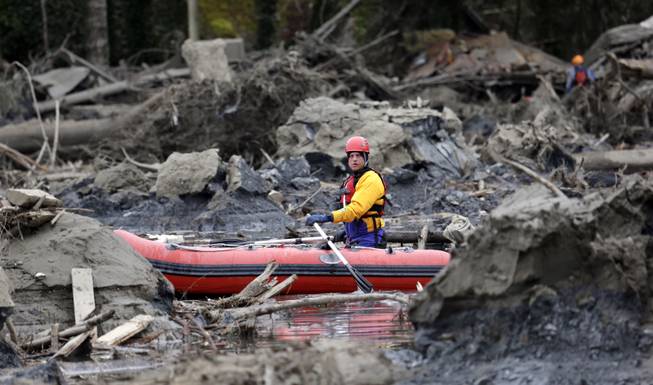A searcher uses a small boat to look through debris from a deadly mudslide Tuesday, March 25, 2014, in Oso, Wash. At least 14 people were killed in the 1-square-mile slide that hit in a rural area about 55 miles northeast of Seattle on Saturday. Several people also were critically injured, and homes were destroyed. 
