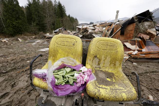 Flowers are left on debris next to a demolished home where a woman's body was found following a deadly mudslide, Tuesday, March 25, 2014, in Arlington, Wash. At least 14 people were killed in the 1-square-mile slide that hit in a rural area about 55 miles northeast of Seattle on Saturday. Several people also were critically injured, and homes were destroyed.