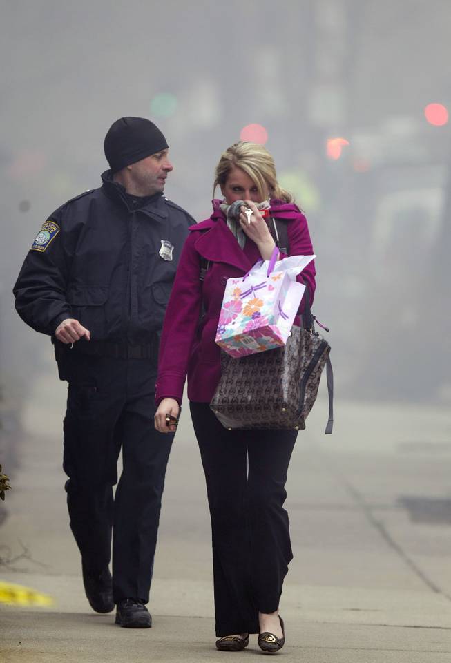 A Boston Police officer escorts a woman away from the scene of a multi-alarm fire at a four-story brownstone in the Back Bay neighborhood near the Charles River, Wednesday, March 26, 2014, in Boston. Boston EMS spokesman Nick Martin says four people, including at least three firefighters, have been taken to hospitals. 