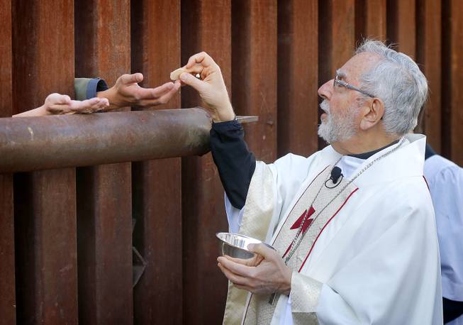 Most Reverend Gerald F. Kicanas, Bishop of Tucson, offers communion to people on the Mexican side of the international border, Tuesday, April 1, 2014, in Nogales, Ariz.